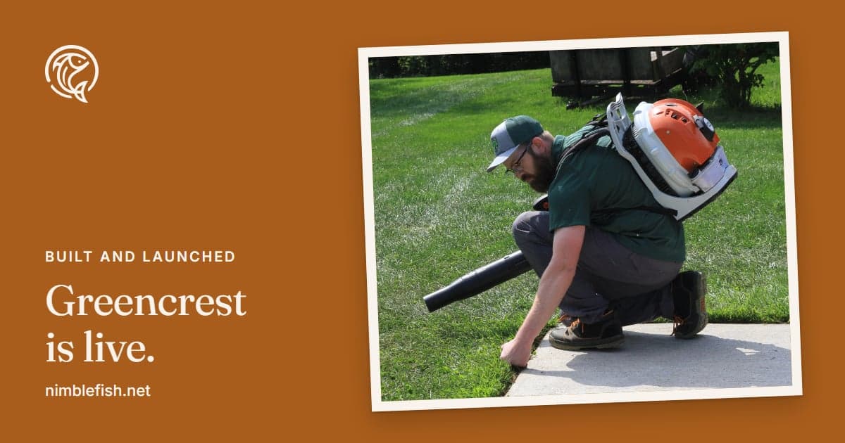Chris Kurtzhals of Greencrest Lawn Care, in his cap and polo with a backpack blower on, crouched at the edge of a lawn, one hand on the grass where it meets the sidewalk.